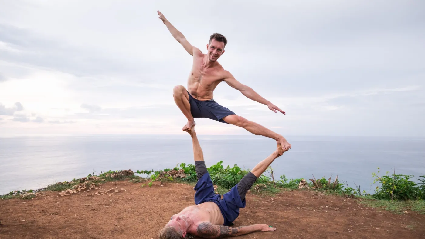 Two people in an AcroYoga pose on a cliff above the sea