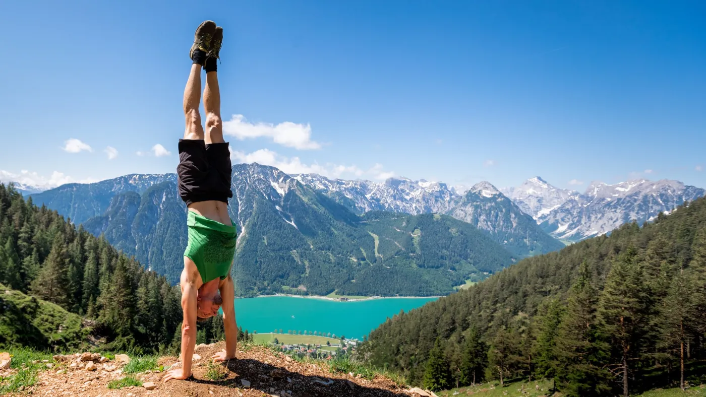 Mito in a handstand above a turquoise mountain lake